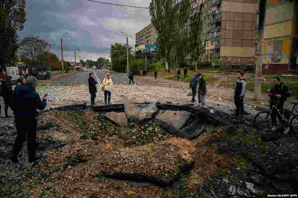 Люди дивляться на вирву, що утворилася внаслідок влучення російської ракети в одну із вулиць Дніпра. 10 жовтня 2022 року. Президент Росії Володимир Путін назвав ракетний терор проти українських міст «відплатою» за пошкодження Керченському мосту, що з'єднує Росію з анексованим нею у 2014 році Кримом. Білий дім стверджує, що масована ракетна атака на міста України планувалася давно.